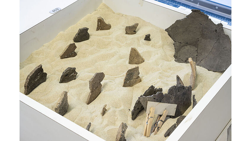 Restoring pottery fragments, glued pieces in a box filled with sand